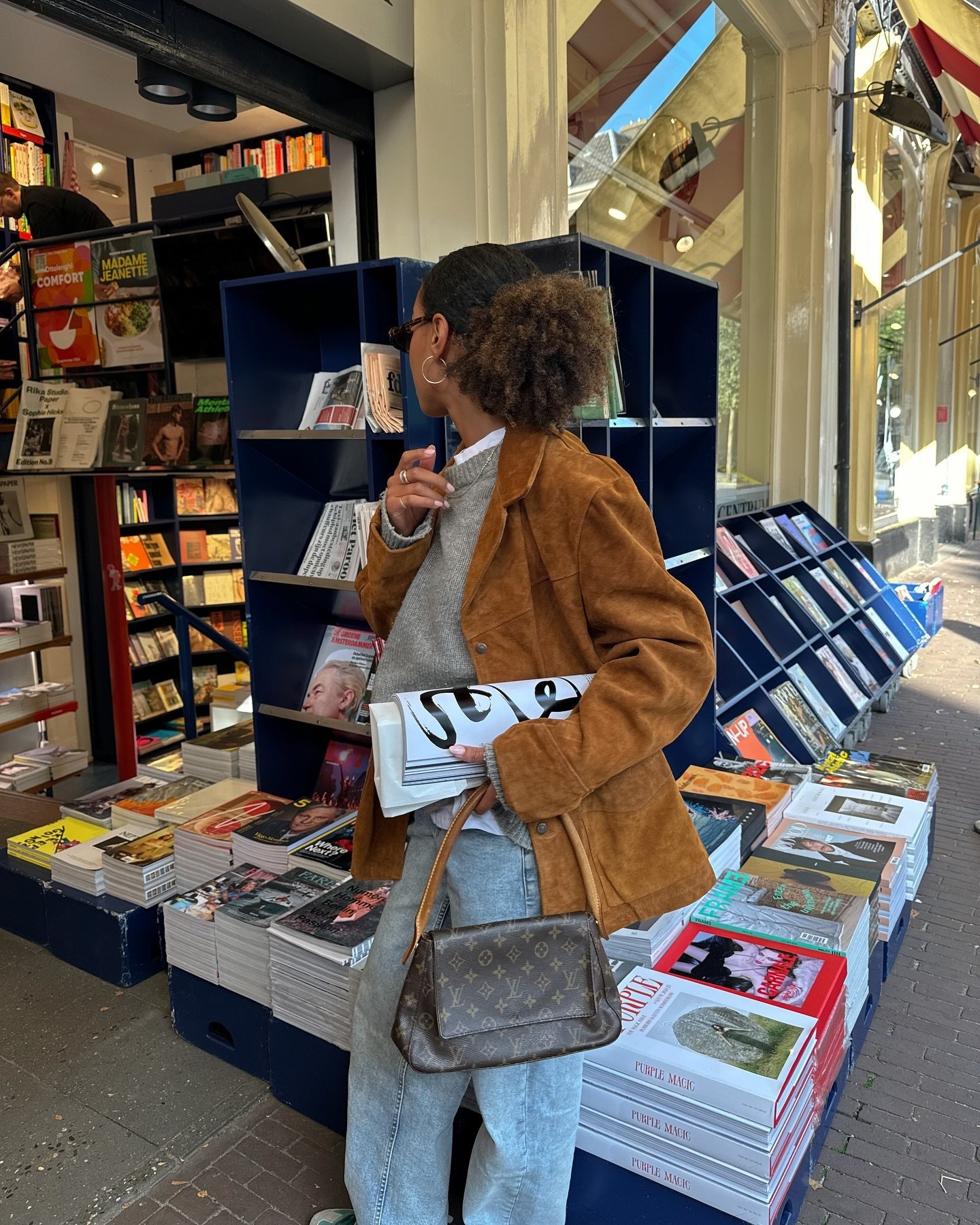 Pessoa vestindo jaqueta de camurça em frente a uma banca de revistas.