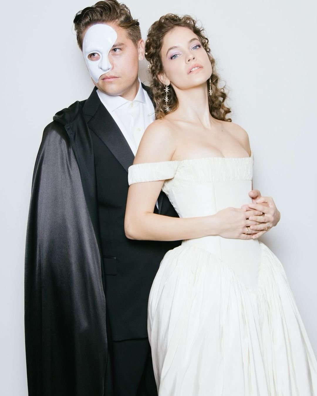 Casal em trajes de gala, com máscara no rosto do homem. Estilo inspirado no Halloween 2024.