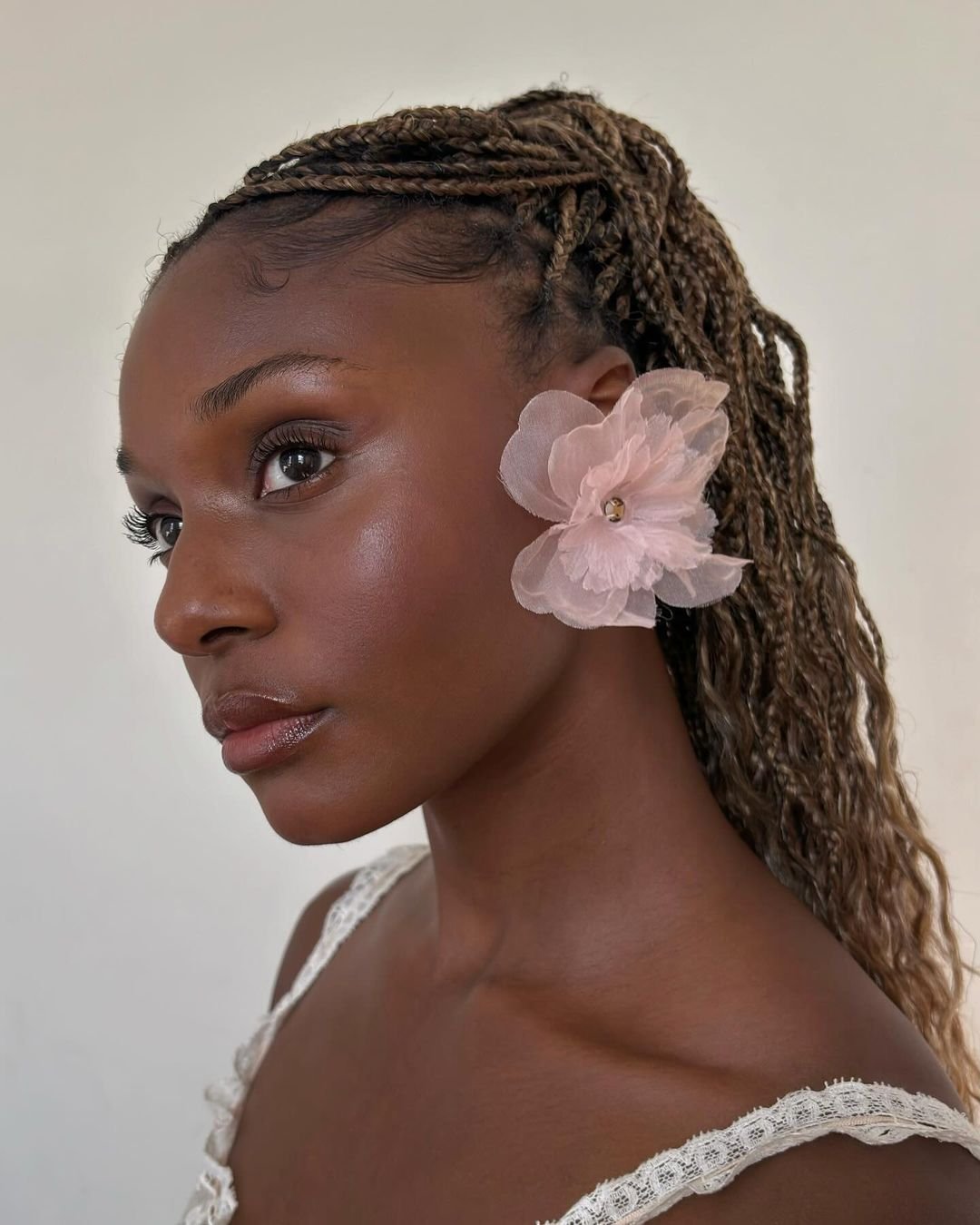 Mulher com tranças e flor rosa no cabelo, maquiagem suave e elegante, ideal para make para festa.