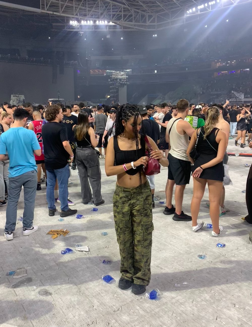 Mulher com calça camuflada e top preto em show lotado. Moda casual com influências militares. Estilo descontraído e urbano. Favela.