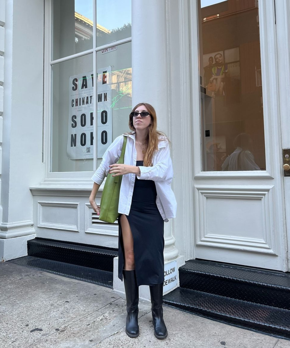 Mulher com óculos escuros e estilo pessoal sofisticado, usando roupa elegante em frente a uma vitrine.