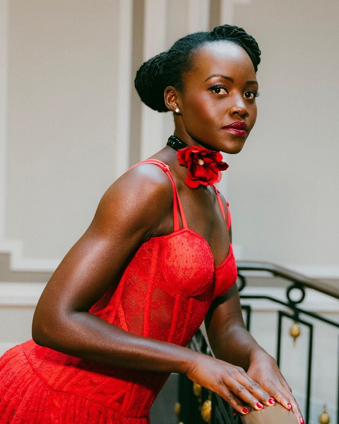 Mulher vestindo um vestido vermelho de renda com alças finas, combinado com um choker floral. Estilo elegante e sofisticado, destacando tendências em moda com textura rendada e acessórios chamativos. penteados para cabelo cacheado elaborado