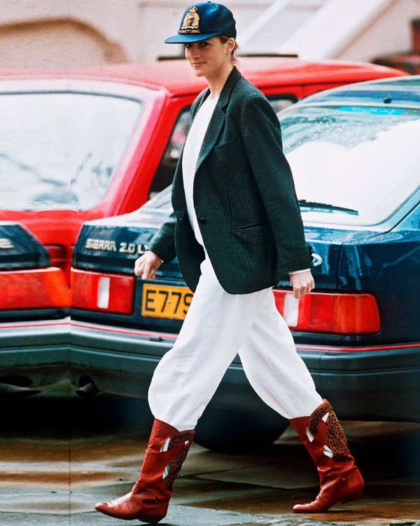 Pessoa andando na rua com blazer, calças soltas, botas vermelhas e boné, em estilo clássico dos anos 80.