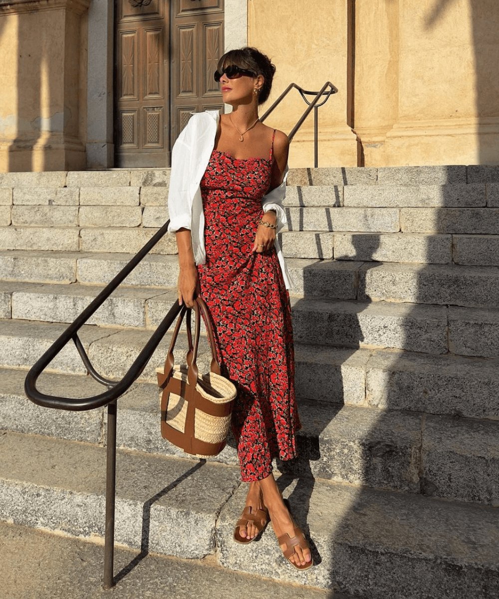 Mulher em vestido floral vermelho nas escadas, usando sandálias e bolsa. Não há sapatos chiques na imagem.