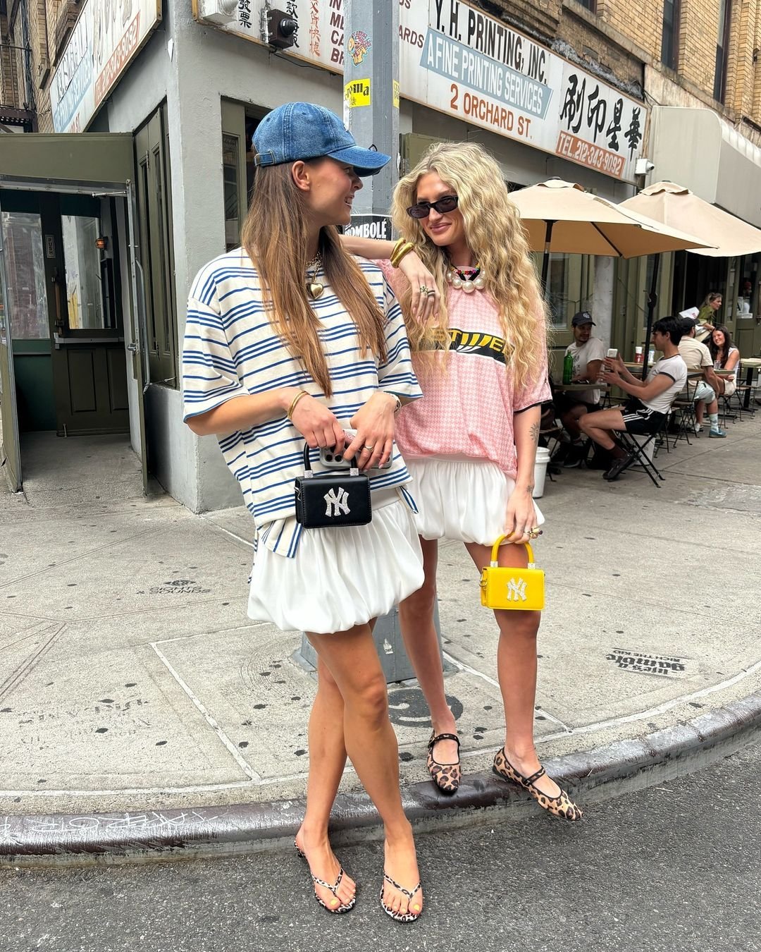 Duas mulheres em uma rua urbana, vestindo roupas estilosas e descontraídas. Ambas usam sapatos tendência. 