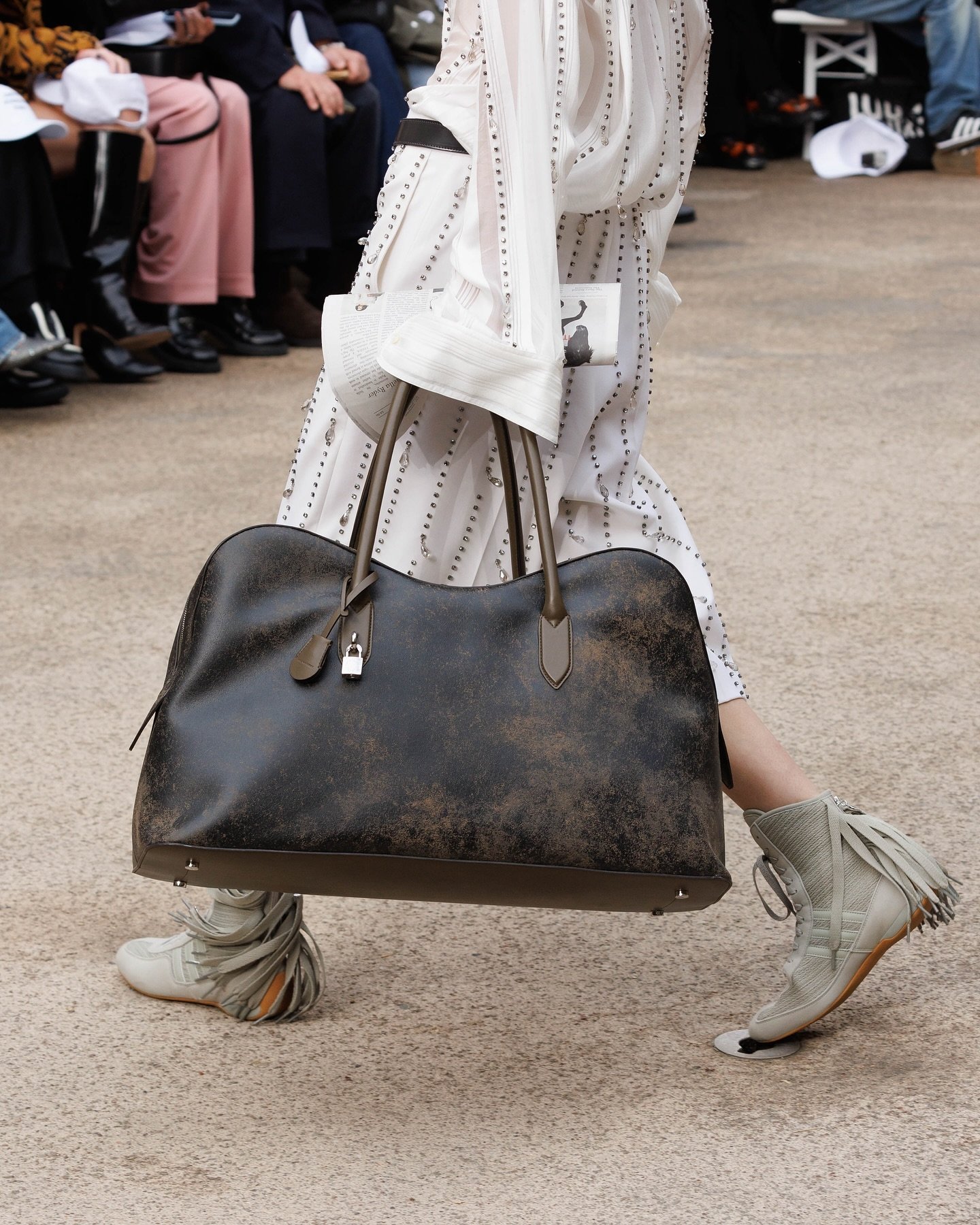 Desfile de moda, bolsa grande em destaque e botas estilo boxing boots cinzas com detalhes de tiras.