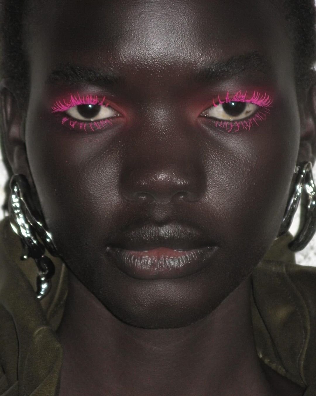 Makeup ousado com cílios rosa neon, tendência vibrante na moda. Acessórios grandes em prata adicionam um toque moderno e futurista ao visual. Estilo destacando contrastes fortes e detalhes chamativos. tendências de beleza primavera/verão 2025
