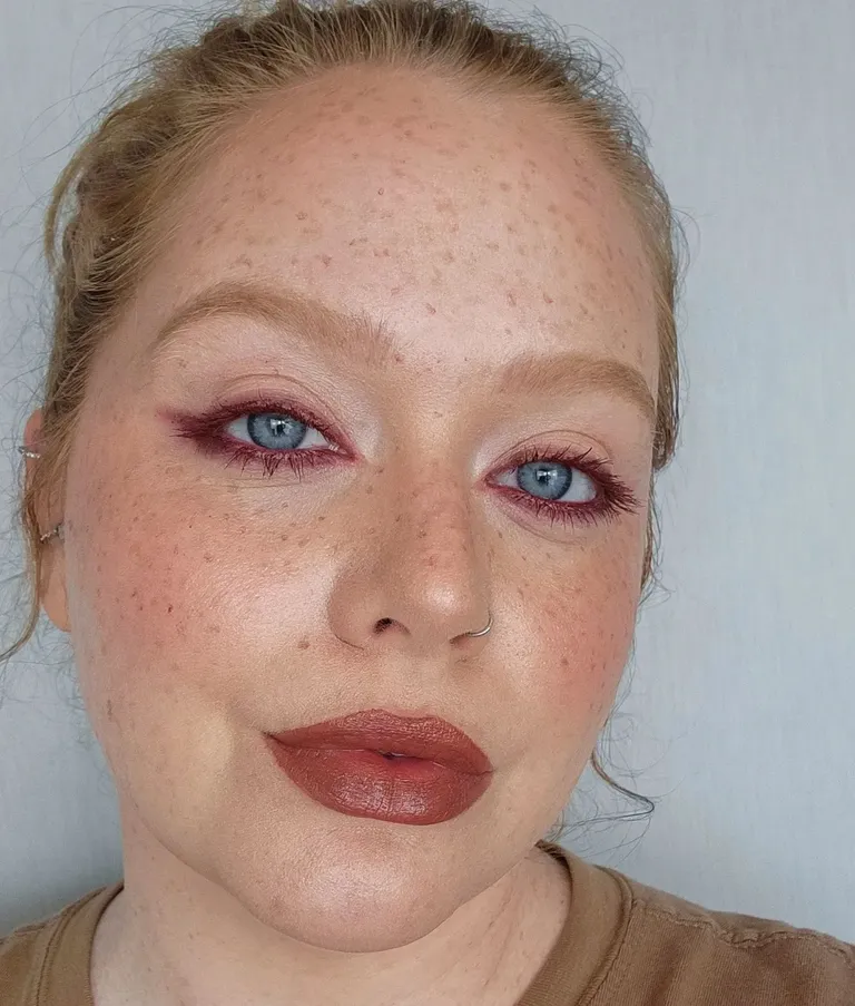 Makeup destacando tendência de olhos com delineador vermelho, sombras suaves e pele com acabamento natural. Batom marrom queimado completa o visual, seguindo a moda de maquiagem focada em tons terrosos e look minimalista. tendências de maquiagem do verão