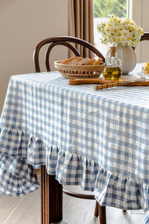 Toalha de mesa xadrez azul com babados, trazendo elegância e charme rústico ao ambiente. Combinações como estas são tendência em decoração de interiores, remetendo ao estilo cottagecore, que valoriza o aconchego e a simplicidade.