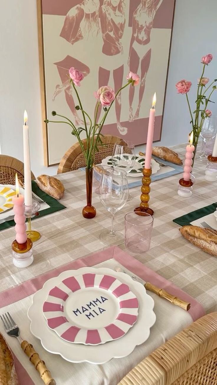 Mesa posta com estética retrô e moderna, destacando pratos listrados, velas decorativas coloridas e louça elegante. Fundo com arte em tons nude e flores que complementam o ambiente sofisticado e convidativo. Ideal para indexação em tendências de decoração.