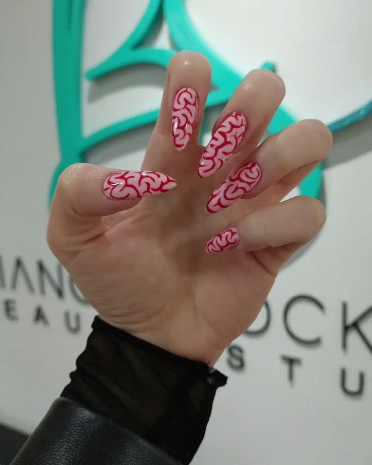 Unhas de halloween com esmalte rosa e design de cérebro em vermelho, combinadas com blusa de tecido transparente preto. Visual ousado e criativo, destacando-se em tendências de nail art e moda alternativa.