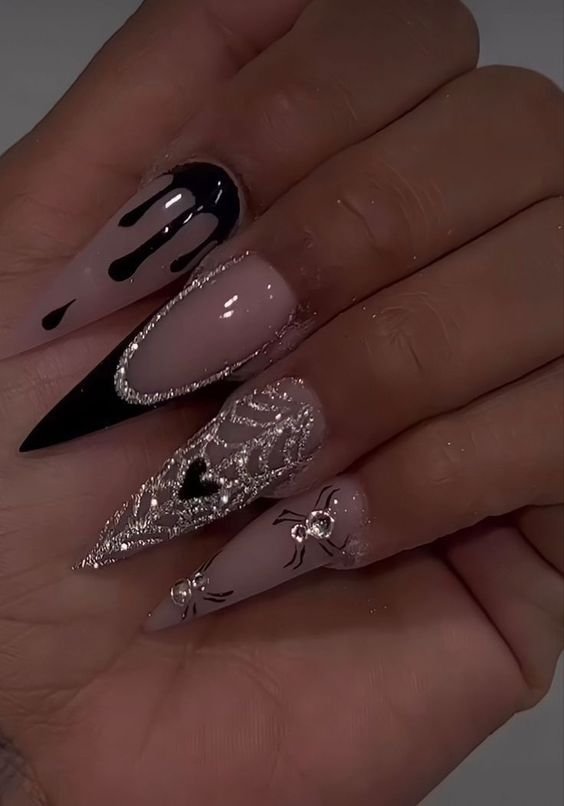 Unhas stiletto com estilo gótico moderno. Design mistura preto e nude, com detalhes em prata e decoração de aranhas. Tendência em nail art que combina elegância e ousadia. Ideal para quem busca expressar criatividade.