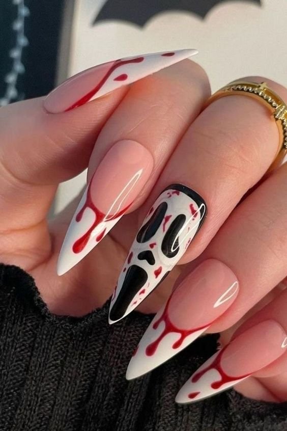 Unhas de halloween com design temático de Halloween, apresentando sangue fake e a icônica máscara de filme de terror. Tendência impactante e criativa, ideal para eventos temáticos ou festas à fantasia, destacando estilo ousado e moderno.