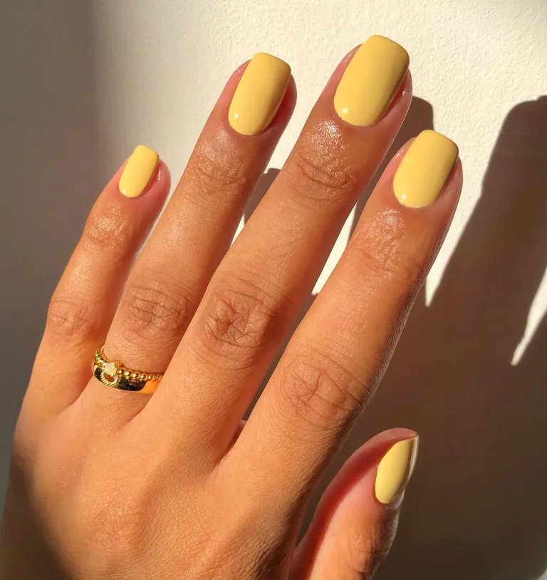 Unhas curtas pintadas de amarelo pastel, tendência de moda moderna para um visual vibrante e estiloso. Acompanha anel dourado minimalista, adicionando um toque elegante e sofisticado. cores de esmalte