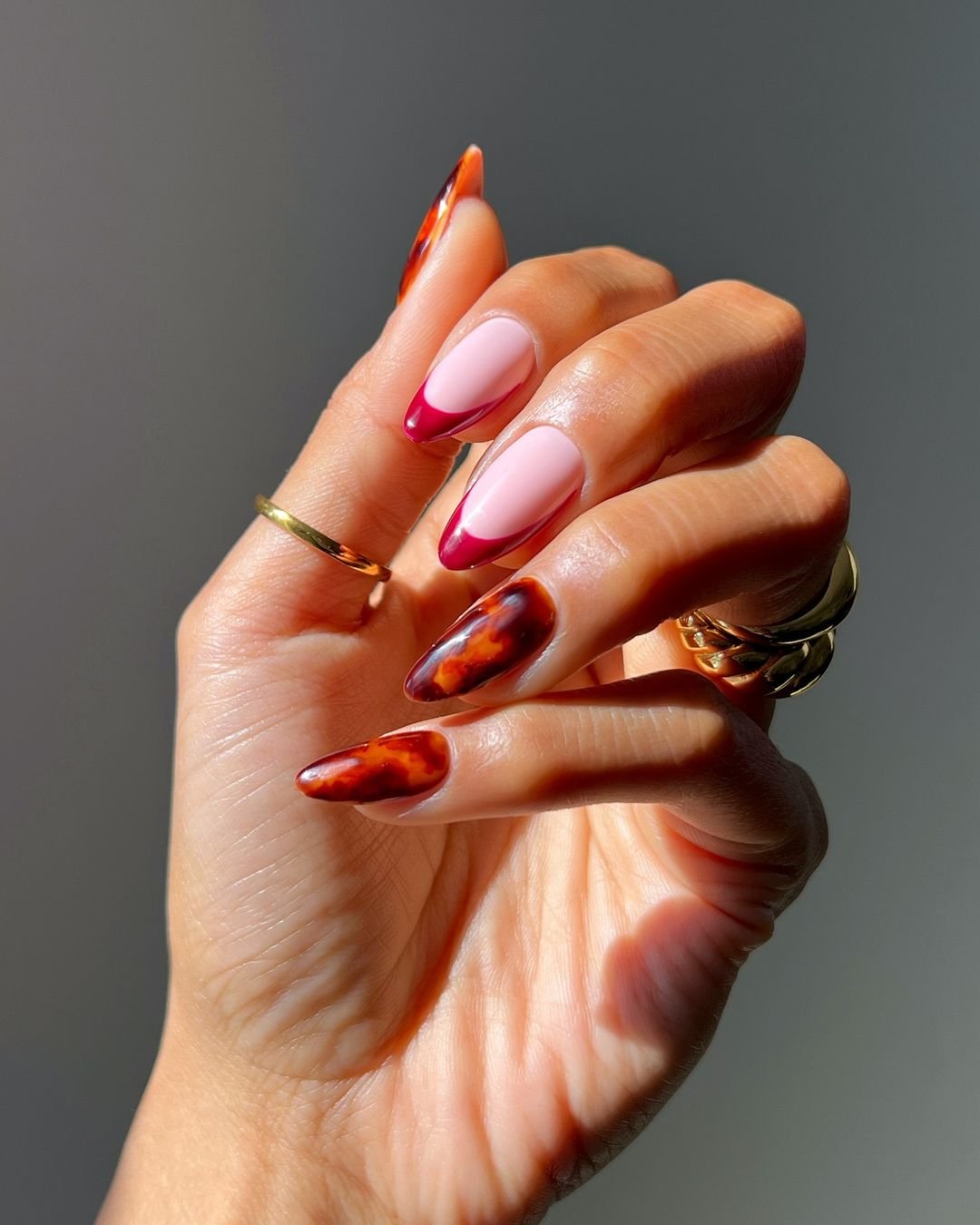 Unhas com design moderno, mesclando francesinha rosa com estampa tartaruga. Anéis dourados minimalistas destacam o estilo sofisticado e tendência de unhas artísticas. cores de esmalte