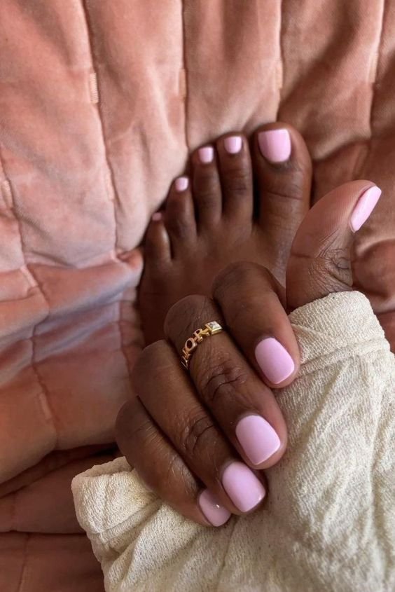 Pés e mãos com unhas pintadas de rosa claro sobre um cobertor rosa. unhas do pé delicadas