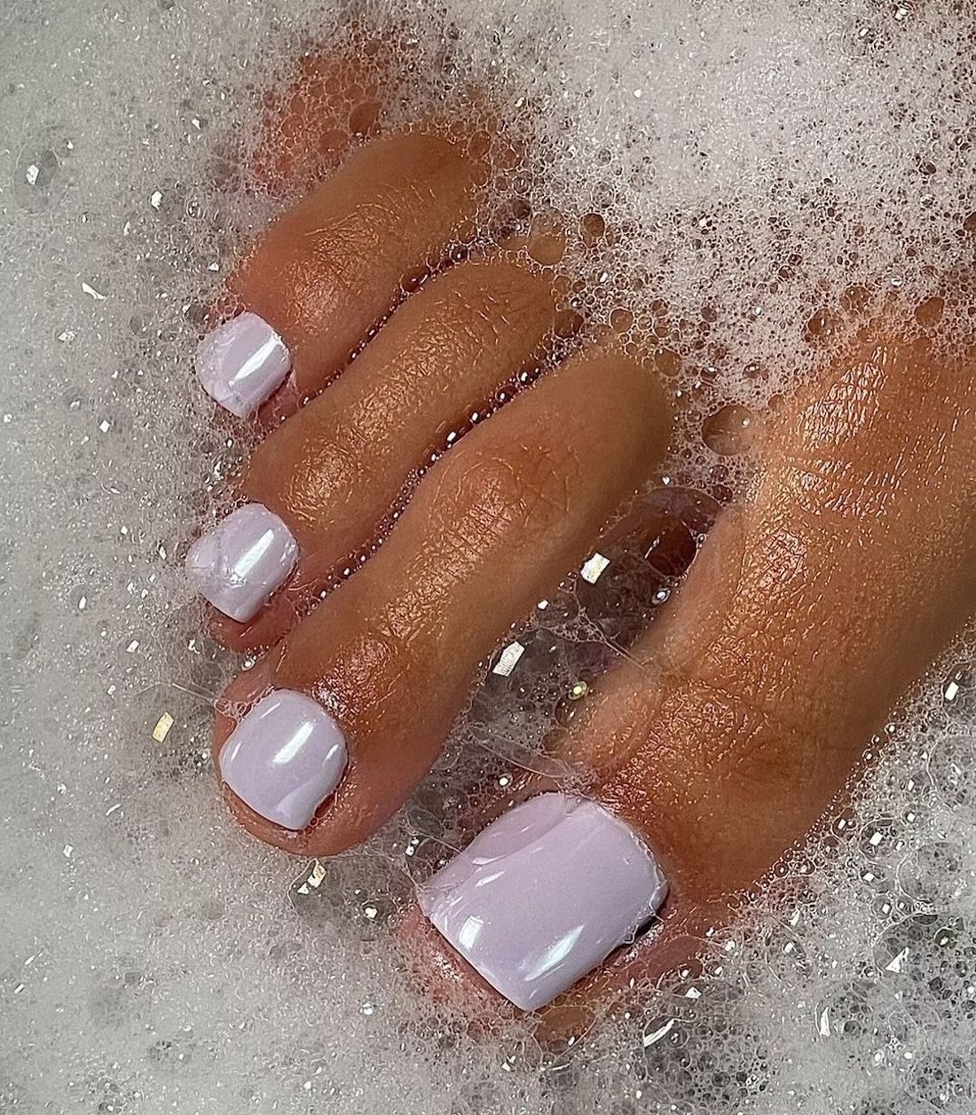 Toes delicadamente pintados em tom claro, imersos em espuma de sabão. unhas do pé delicadas