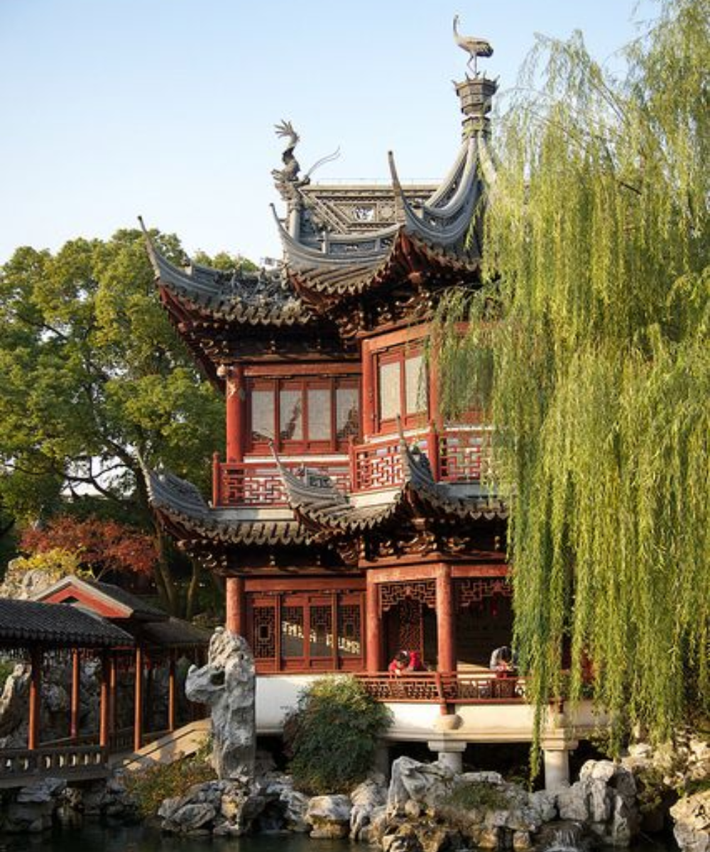 Imagem de um tradicional pavilhão chinês com arquitetura clássica, destacando-se pelo telhado ornamentado e detalhes em madeira. O ambiente reflete uma estética cultural rica, típica de locais históricos na China.