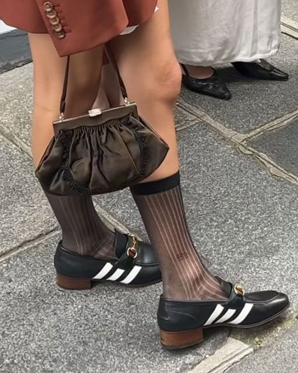 Sapatos com salto baixo e meias transparentes listradas, combinados com bermuda e bolsa marrom em passeio urbano.