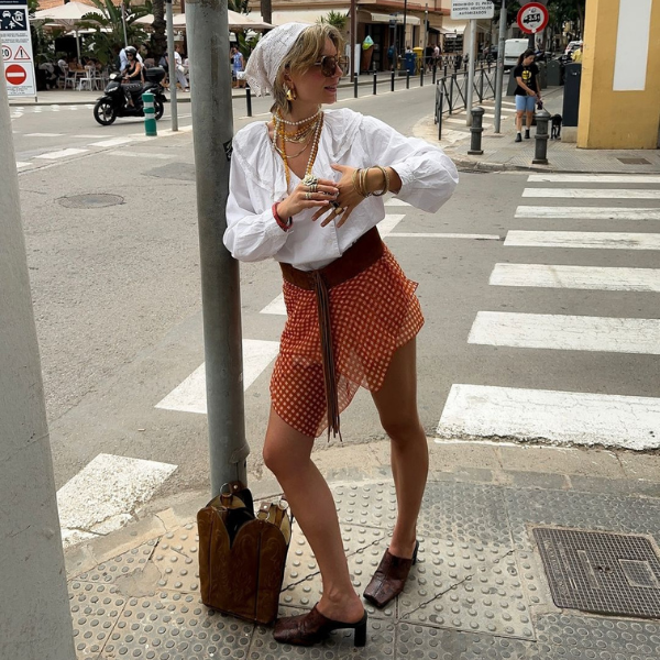 Pessoa com acessórios boho coloridos e roupas leves em uma esquina urbana.