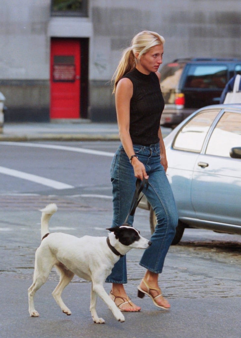 Mulher conduz cachorro na rua, usando blusa preta e jeans, combinando roupas clássicas no visual casual urbano.