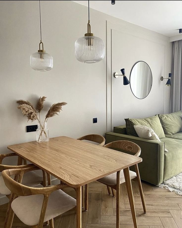 Sala de estar em apartamento pequeno com mesa de madeira, cadeiras, sofá verde e decoração minimalista.