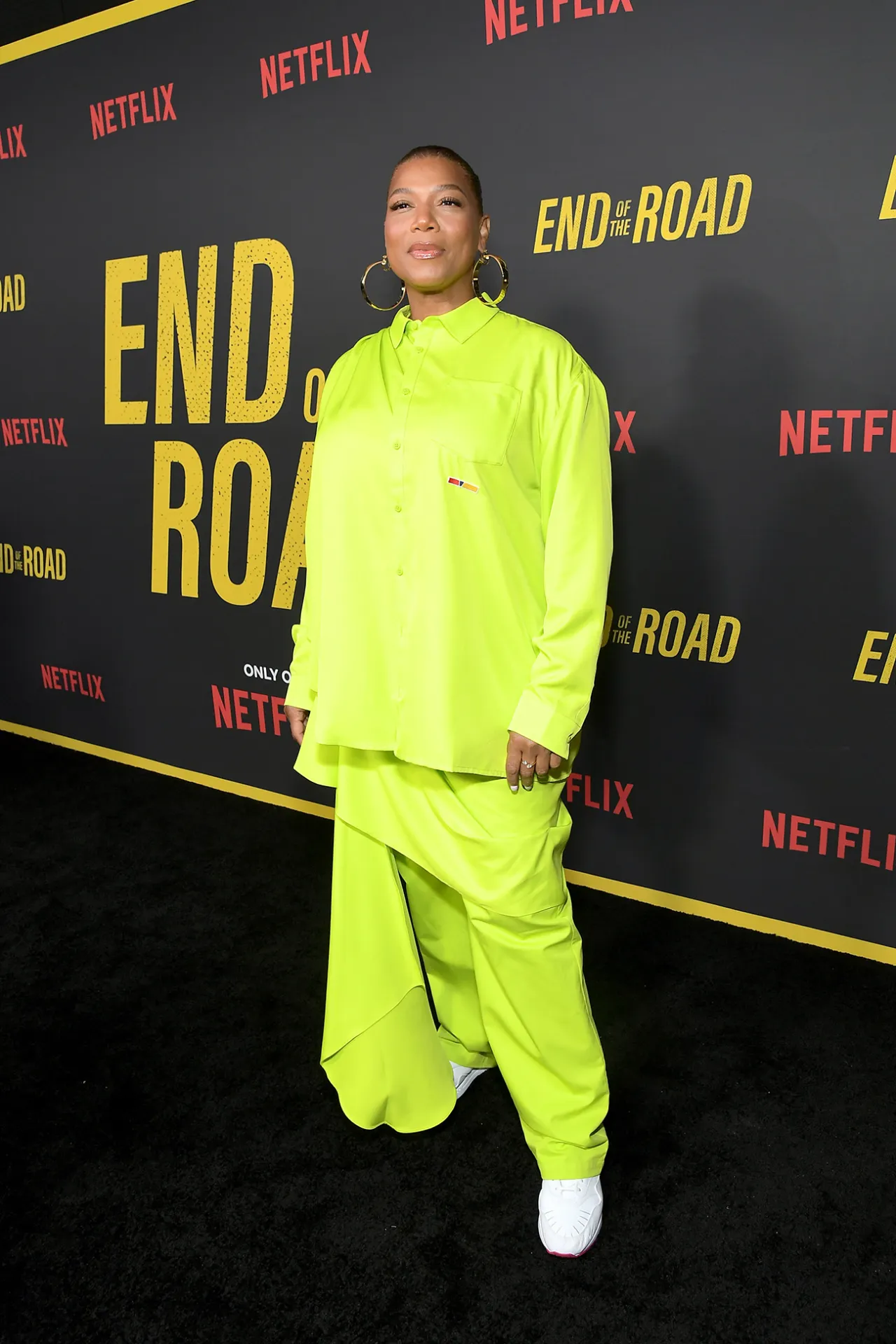 Queen Latifah em um conjunto verde neon com fundo de estreia do filme 