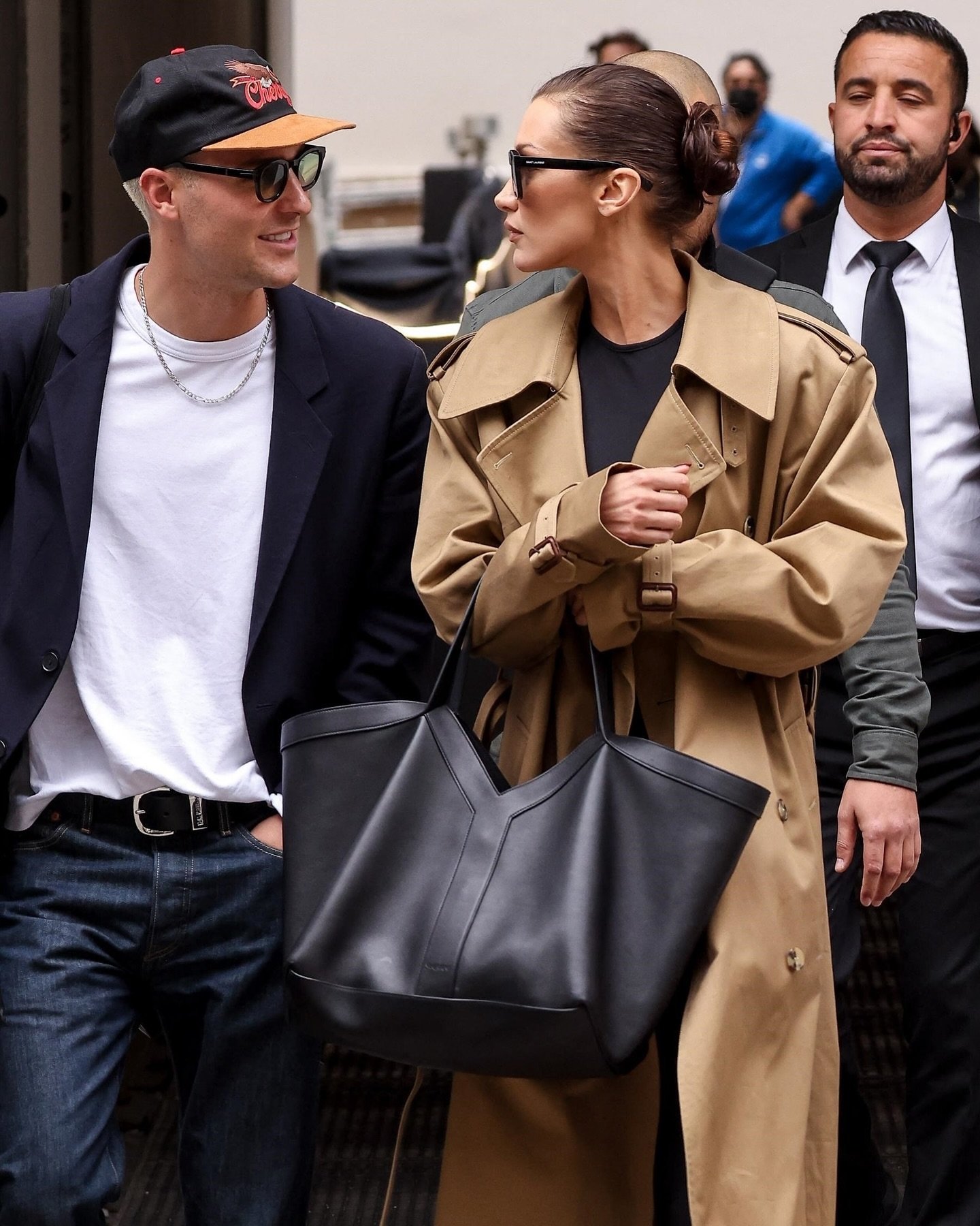 Pessoa usando um casaco bege carrega uma bolsa elegante e estilosa enquanto conversa com outra pessoa.