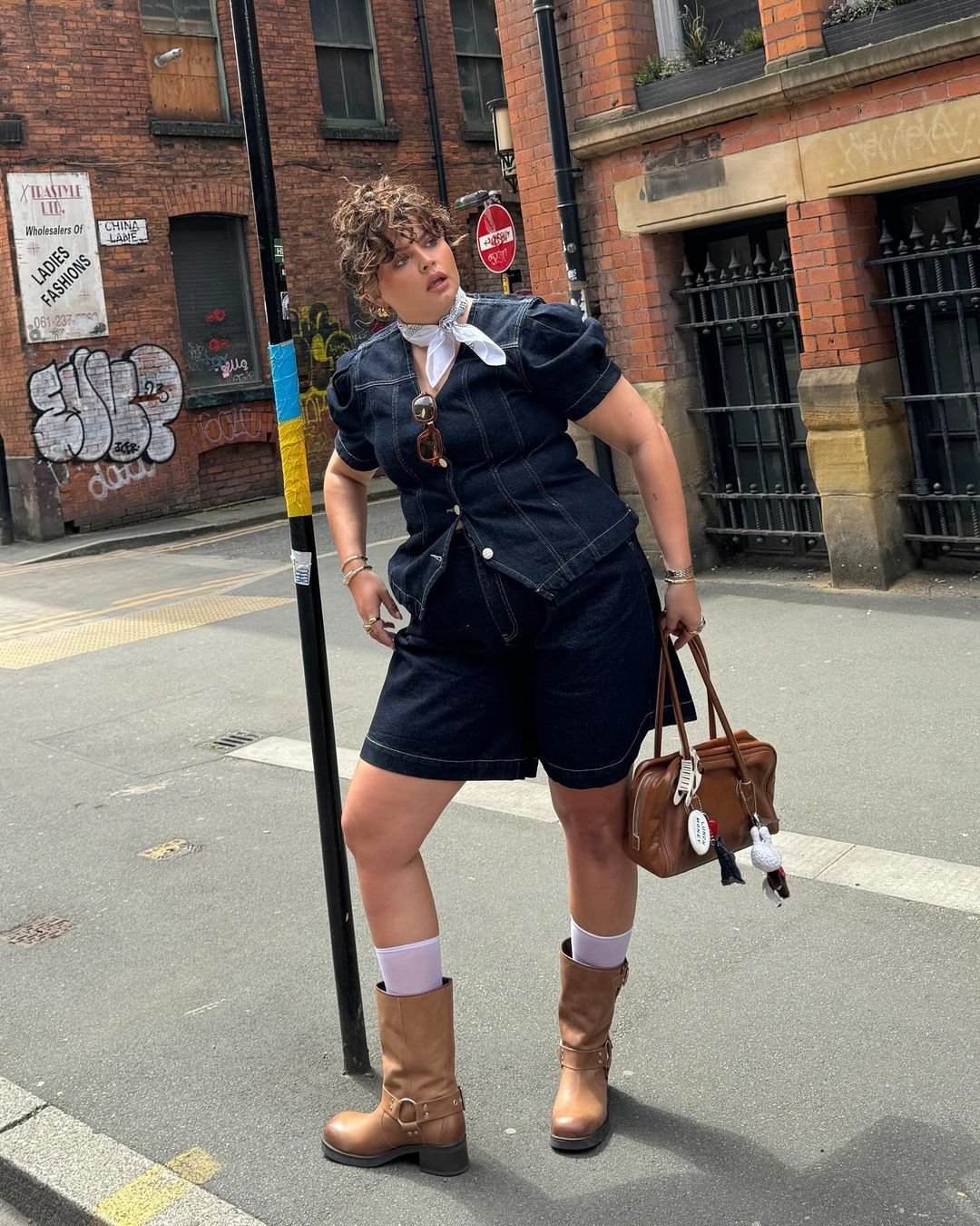 Pessoa usando conjunto jeans e bota de cano alto marrom em uma rua urbana.