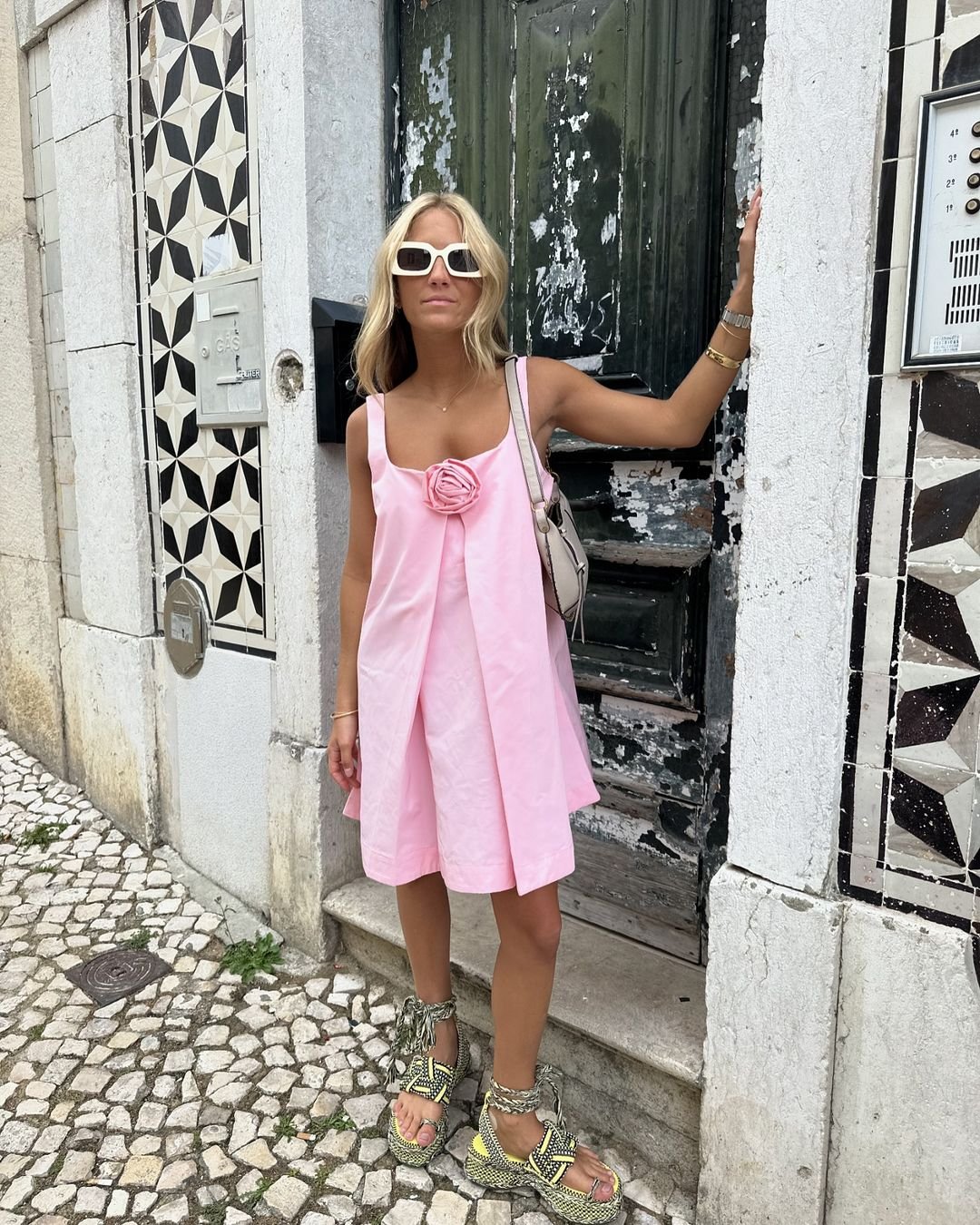 Vestido rosa claro com sandálias, adequado para looks de calor, em frente a uma porta verde desbotada e mural decorativo.