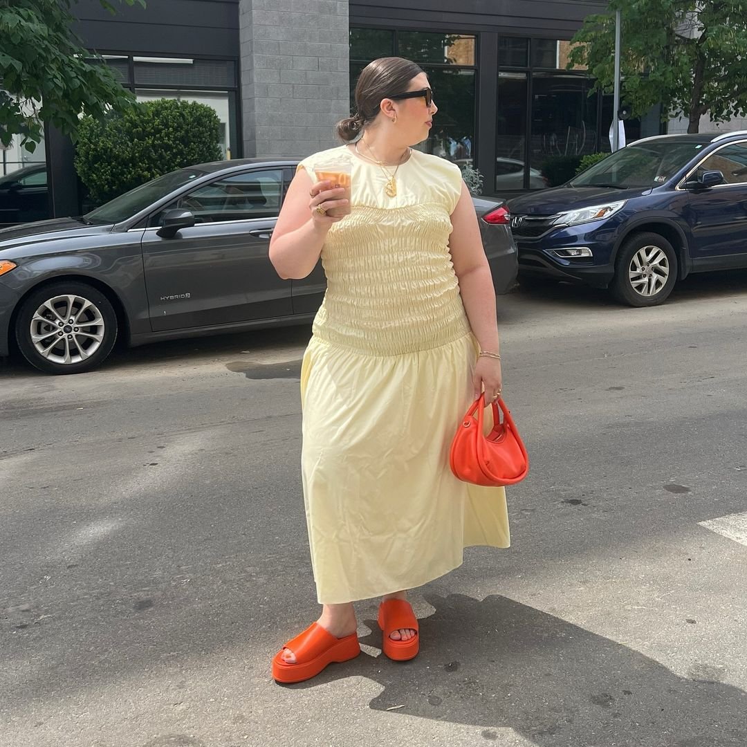 Pessoa com vestido amarelo claro, bolsa e sandálias laranja vibrante, destacando a combinação de cores.