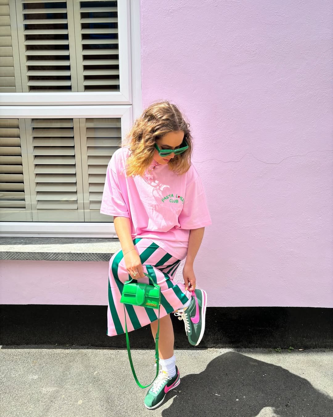 Pessoa vestindo camiseta rosa e saia listrada rosa e verde com óculos e bolsa verde, destacando combinação de cores.