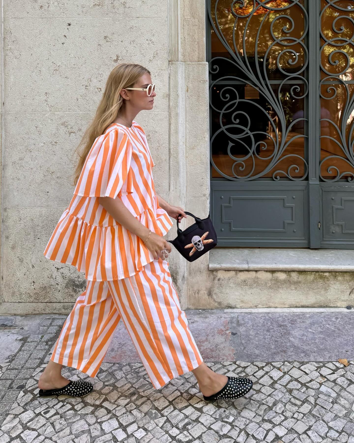 Mulher usando conjunto de listras laranja e branco, bolsa preta com estampa e chinelos pretos.