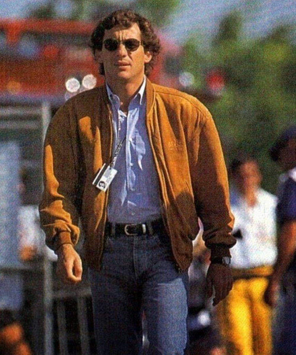 Homem caminhando com jaqueta marrom, camisa azul e óculos escuros, transmitindo confiança e elegância casual.