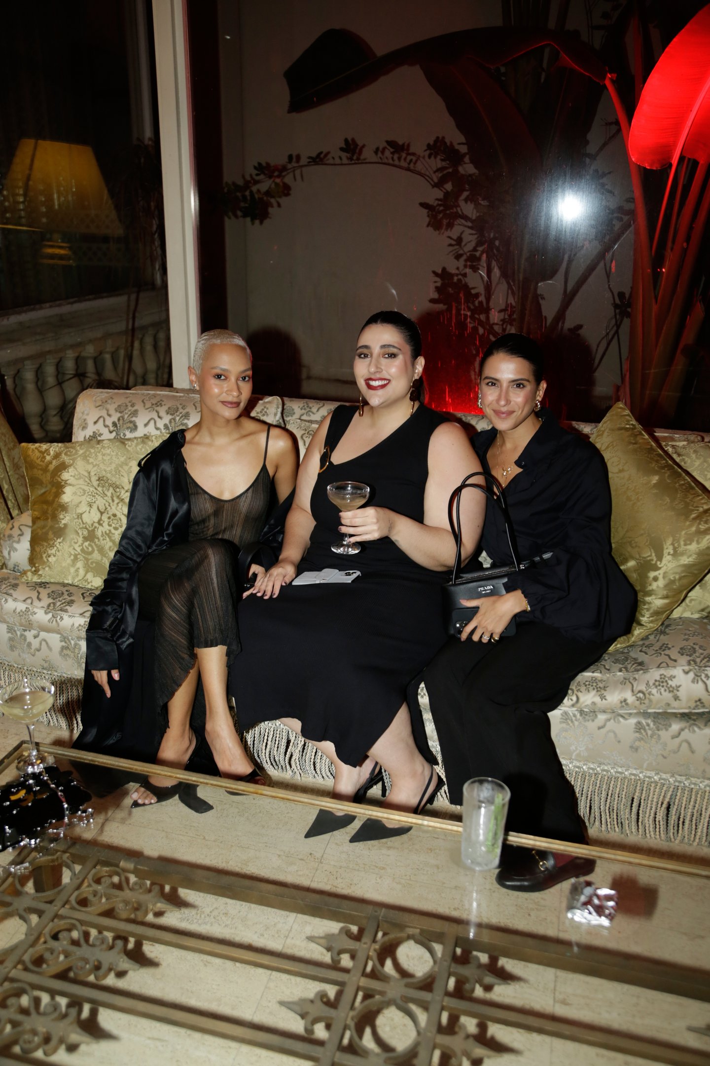 Pessoas sentadas em um sofá elegante em um evento comemorativo aos 30 anos da Nars, segurando bebidas.