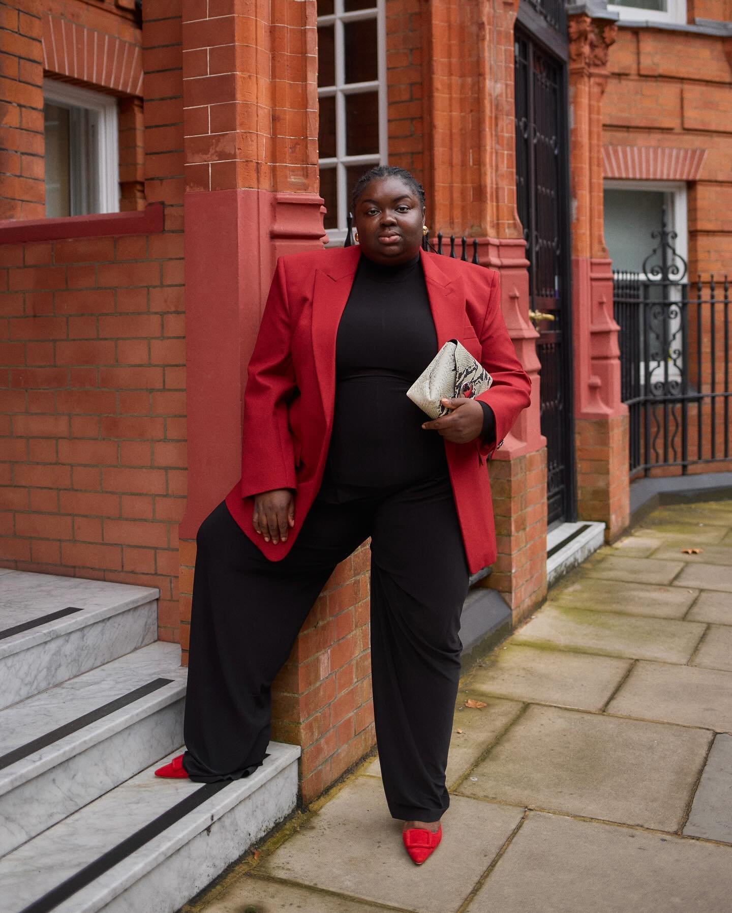 Blazer vermelho e calça preta compõem look elegante para festa da empresa. Mulher segura bolsa.