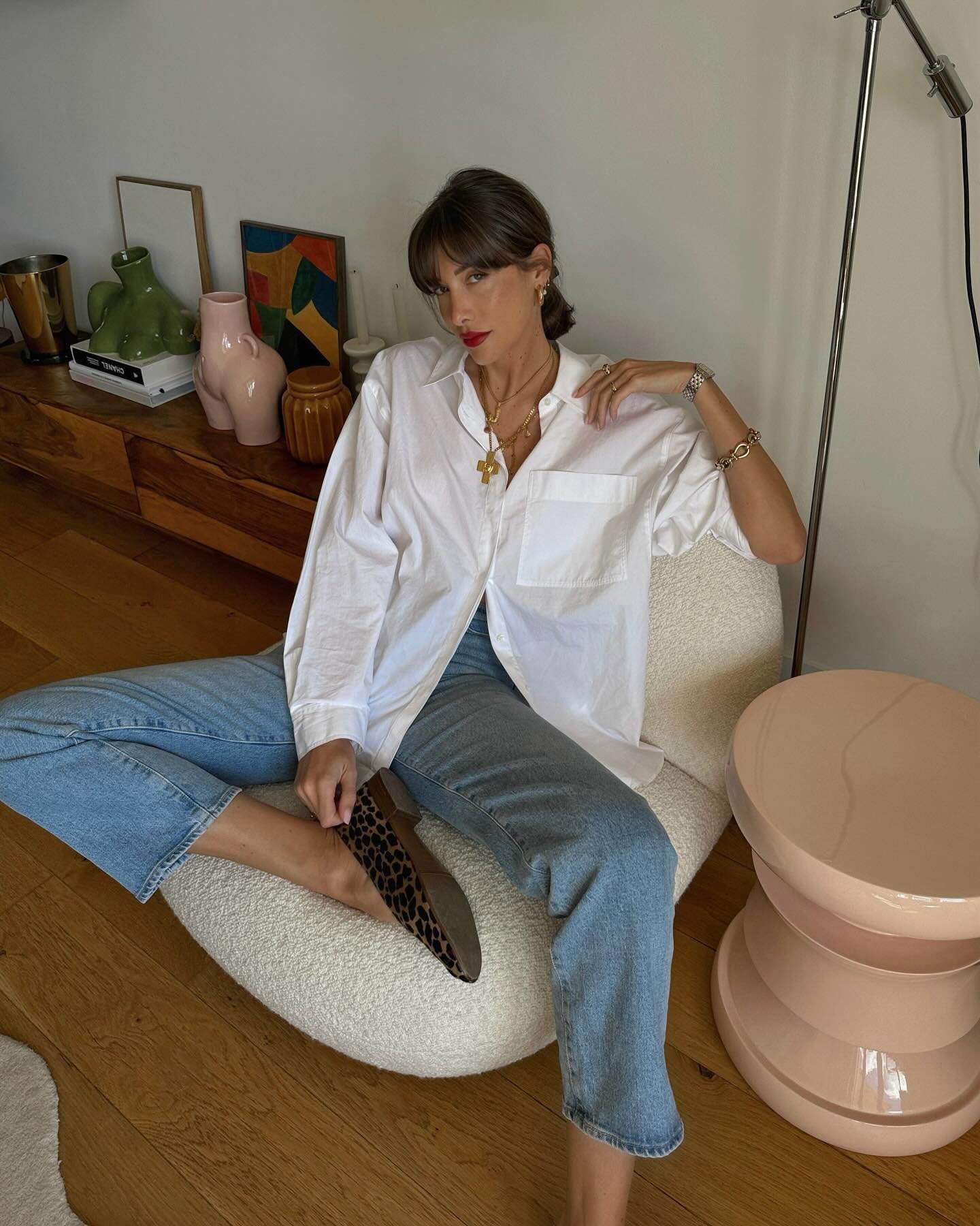 Mulher sentada em cadeira confortável, usando camisa branca e jeans, idealizando um look casual para festa da empresa.