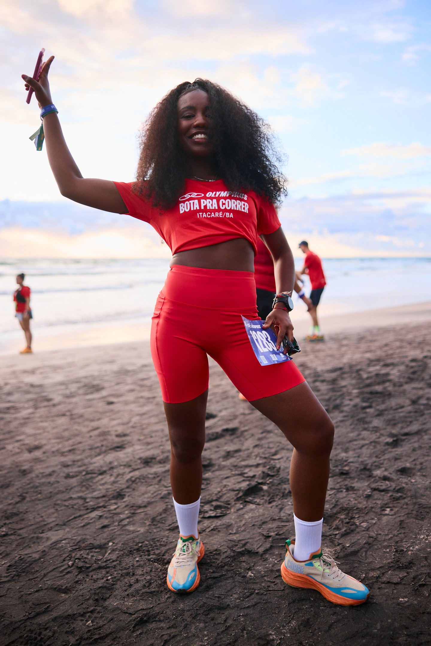 Mulher sorrindo na praia usando roupa esportiva vermelha em uma corrida. Tênis de oncinha.