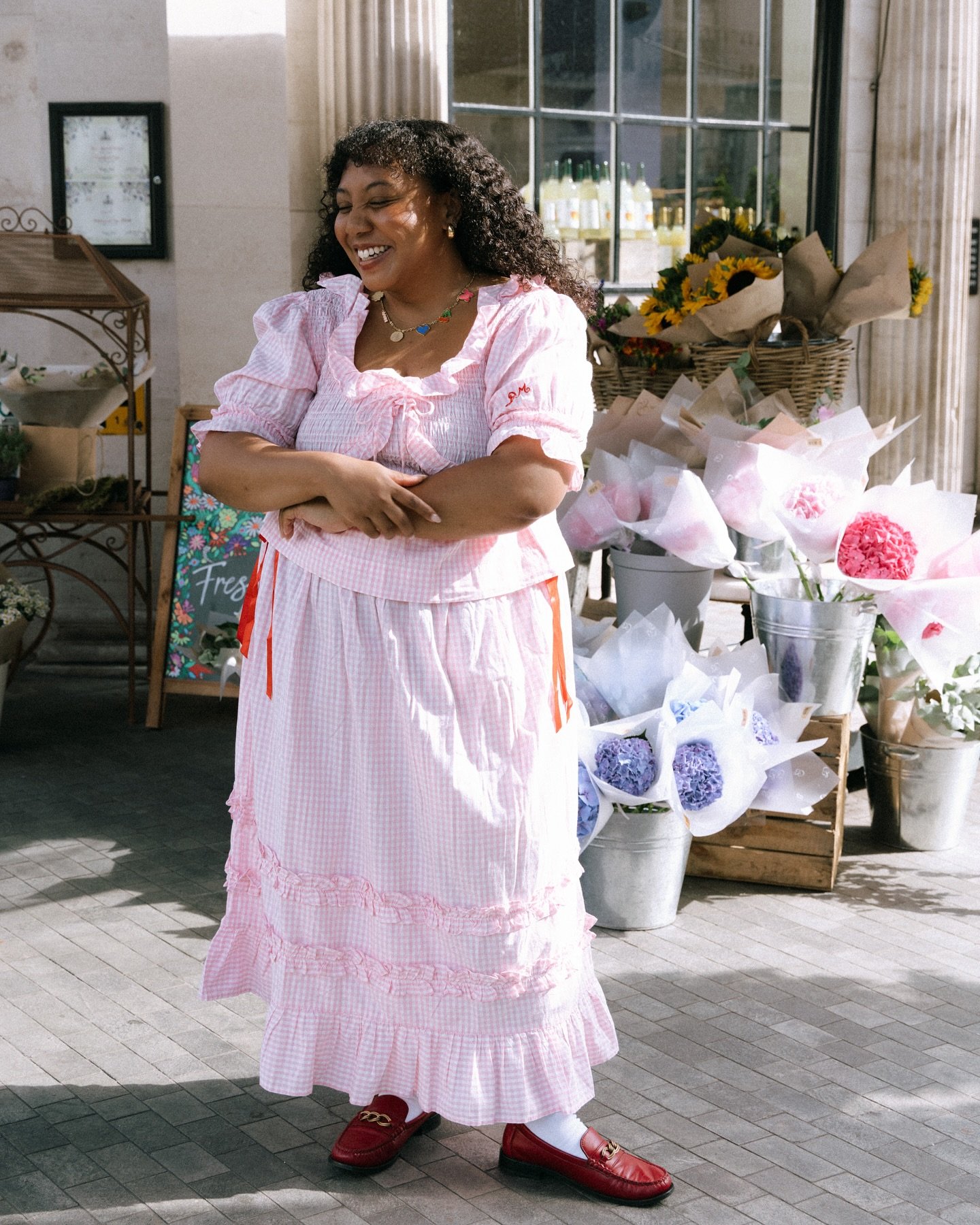 Pessoa sorrindo com vestido rosa claro listrado, em frente a uma loja de flores. Look elegante de verão.