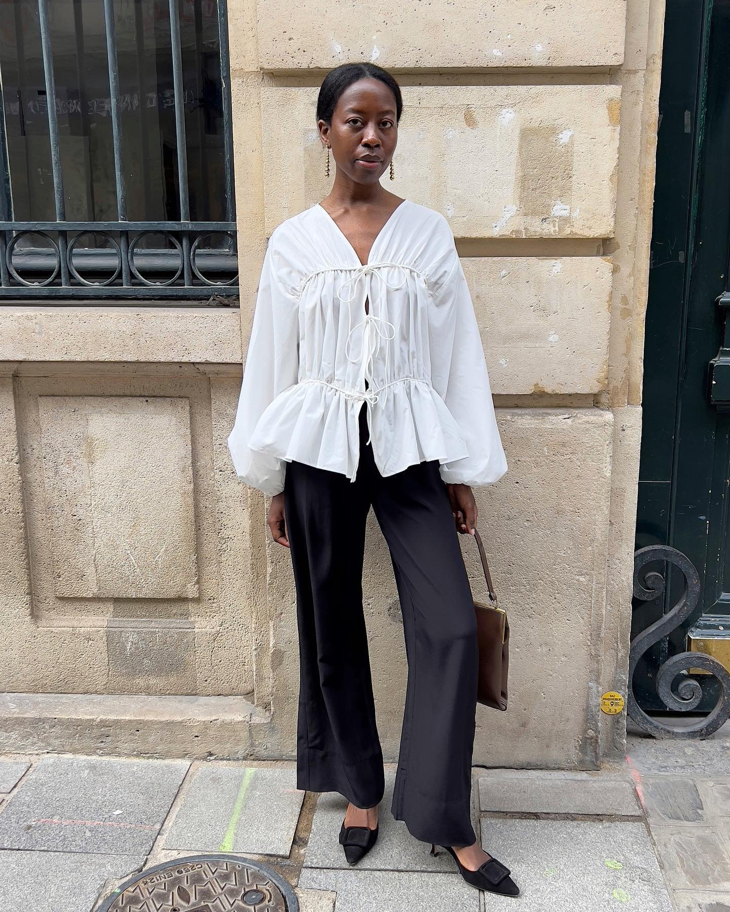 Blusa branca com mangas bufantes e calça preta compõem look elegante de verão em rua de pedra.