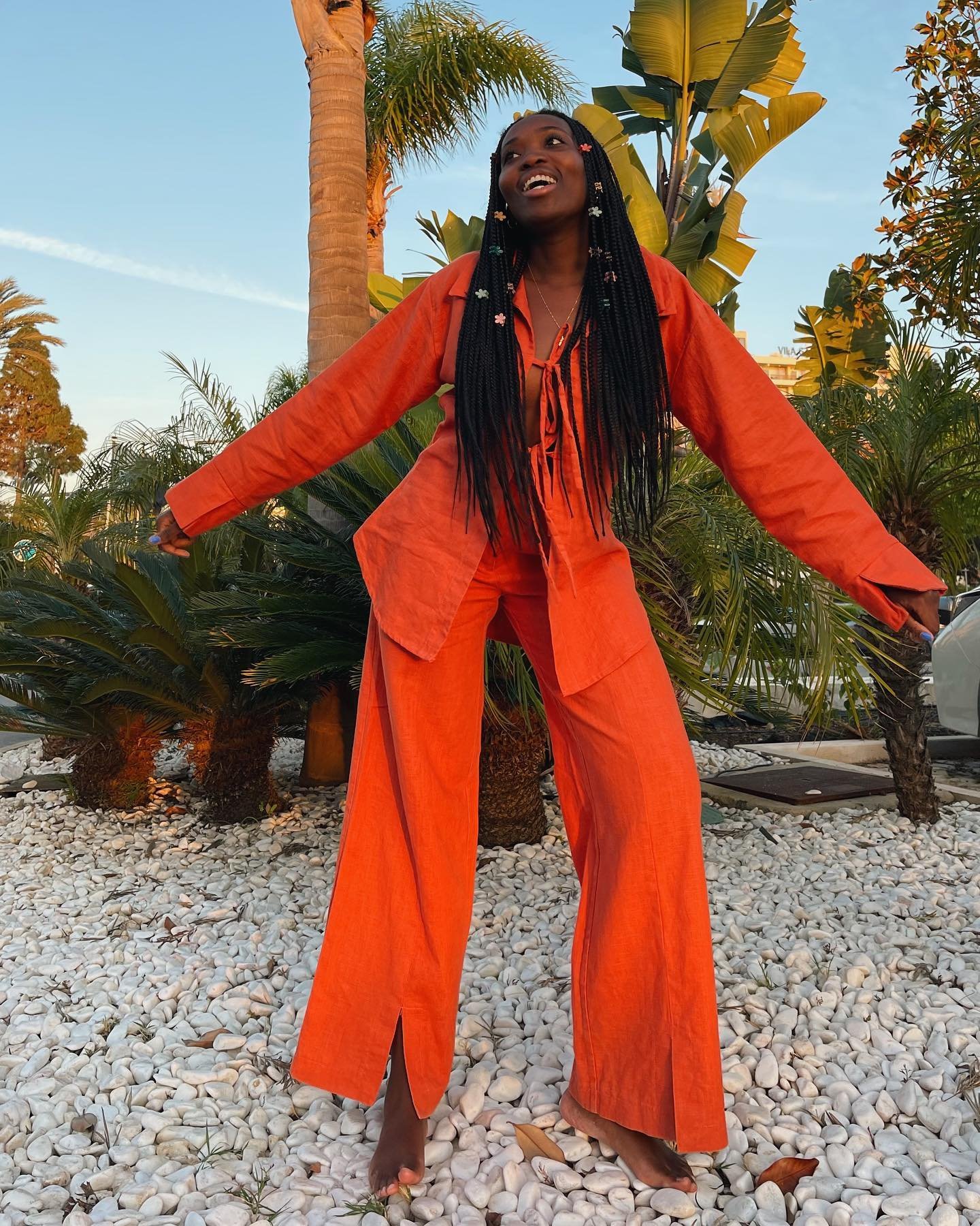 Pessoa com traje laranja vibrante sob palmeiras, exibindo looks elegantes de verão em clima ensolarado.