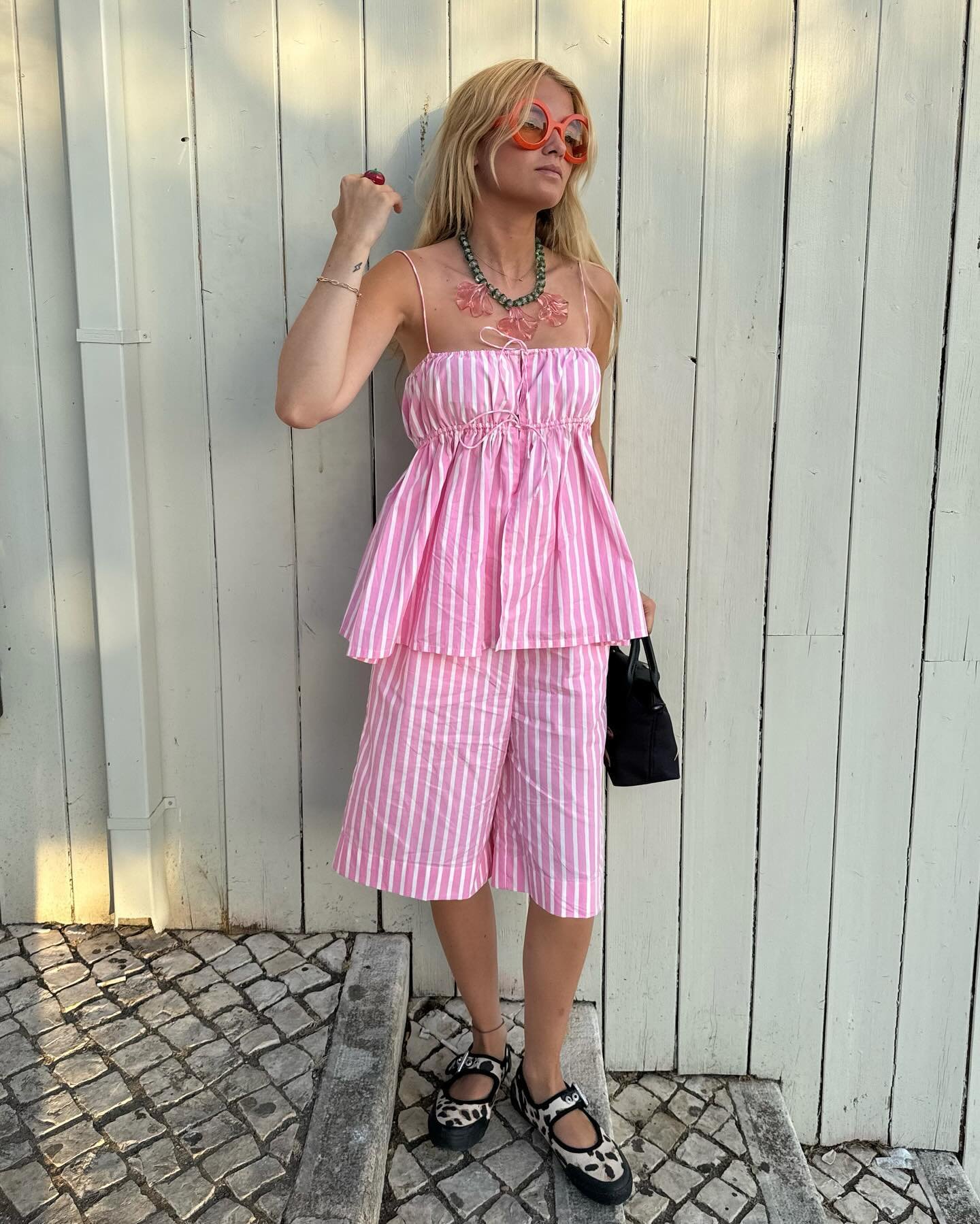 Pessoa usando conjunto listrado rosa e branco, com colar verde, óculos laranja e sapatos estampados, transmite looks elegantes de verão.