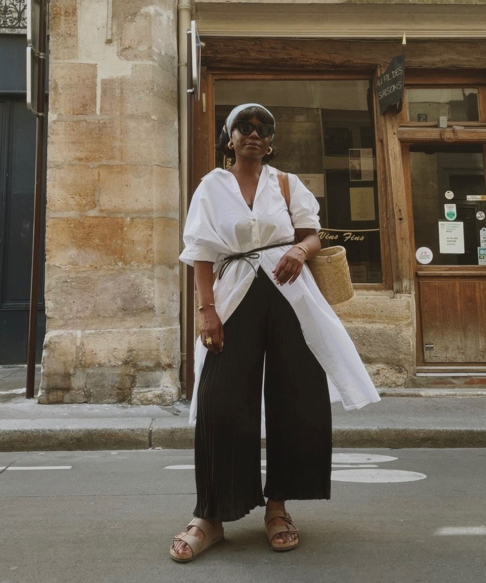 Mulher com camisa branca ampla e calça preta larga, estilo casual. Bolsas de palha. Looks fáceis e bonitos.