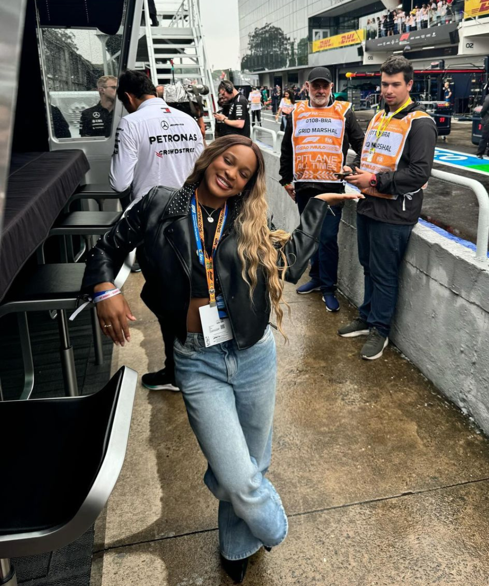 Pessoas em pista de corrida no GP de São Paulo 2024, com marshall ao fundo e mulher sorrindo em destaque.