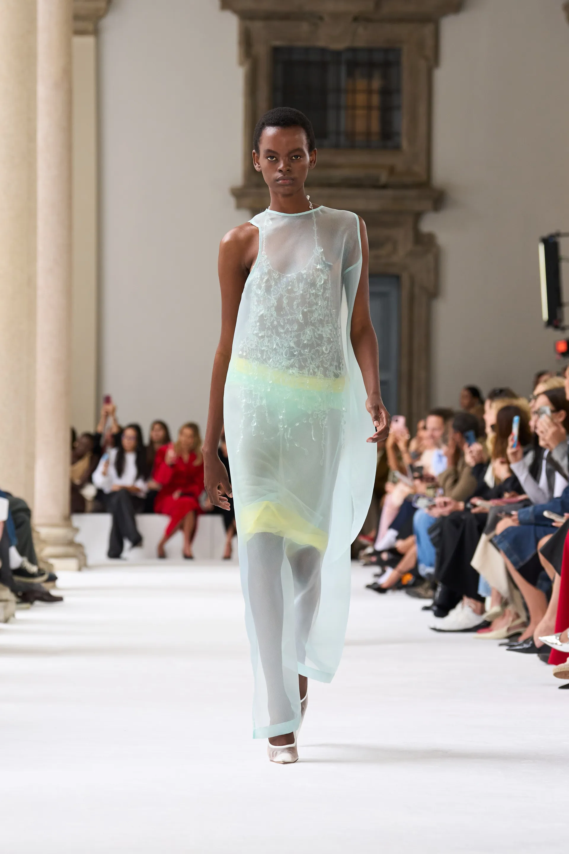 Modelo na passarela com vestido translúcido; tons suaves, tendência nas cores do verão 2025.