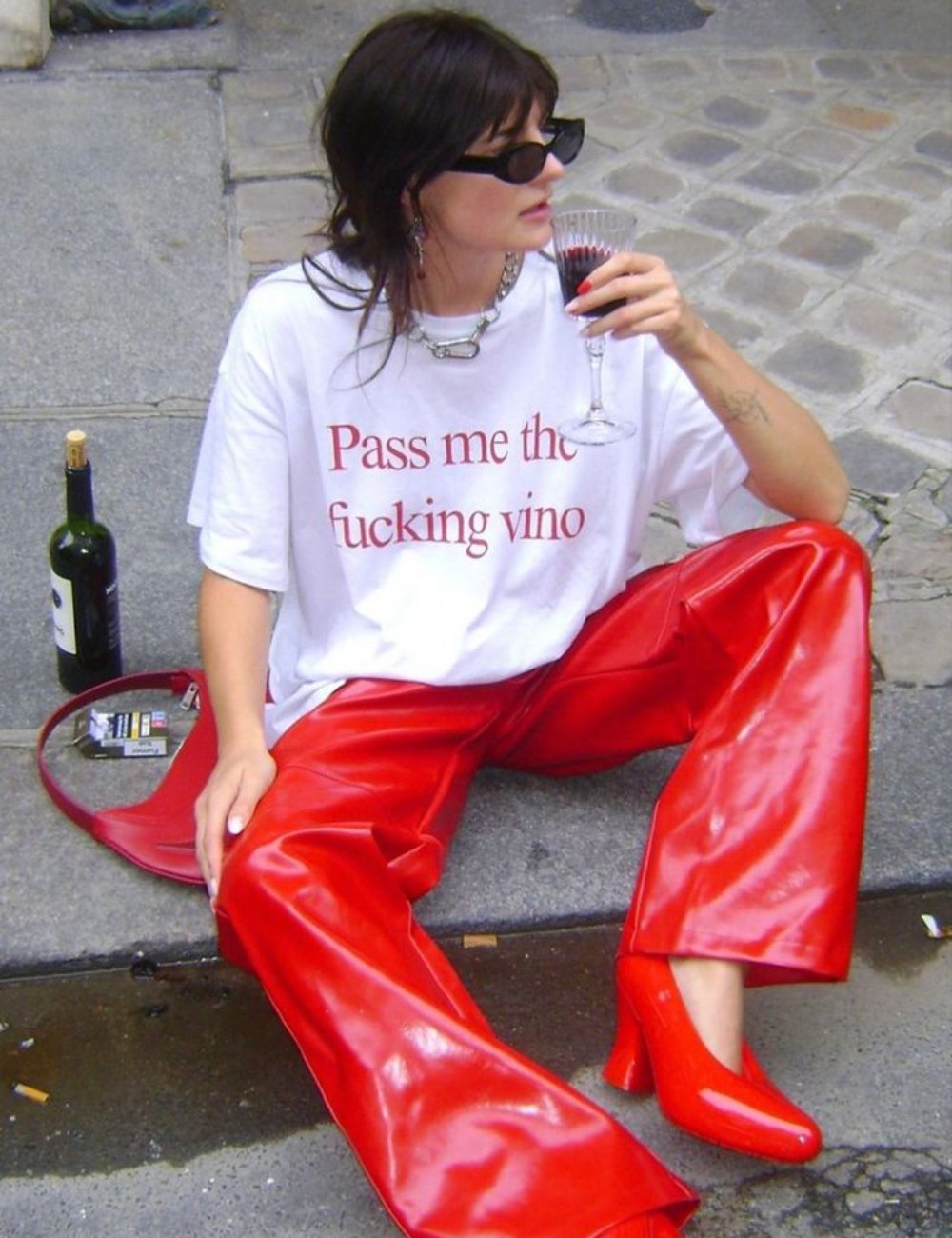 Mulher sentada na calçada, com camisa estampada e calça vermelha, segura uma taça de vinho, evocando Mercúrio retrógrado em sagitário.