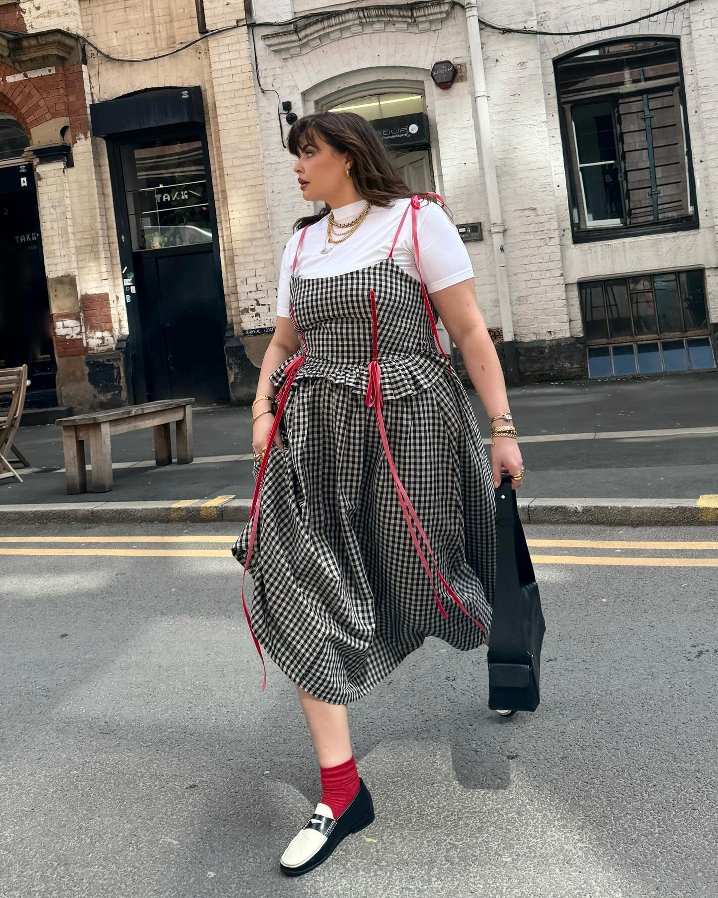 Mulher usando vestido xadrez e loafers bicolores nas ruas. Tendência em moda urbana.