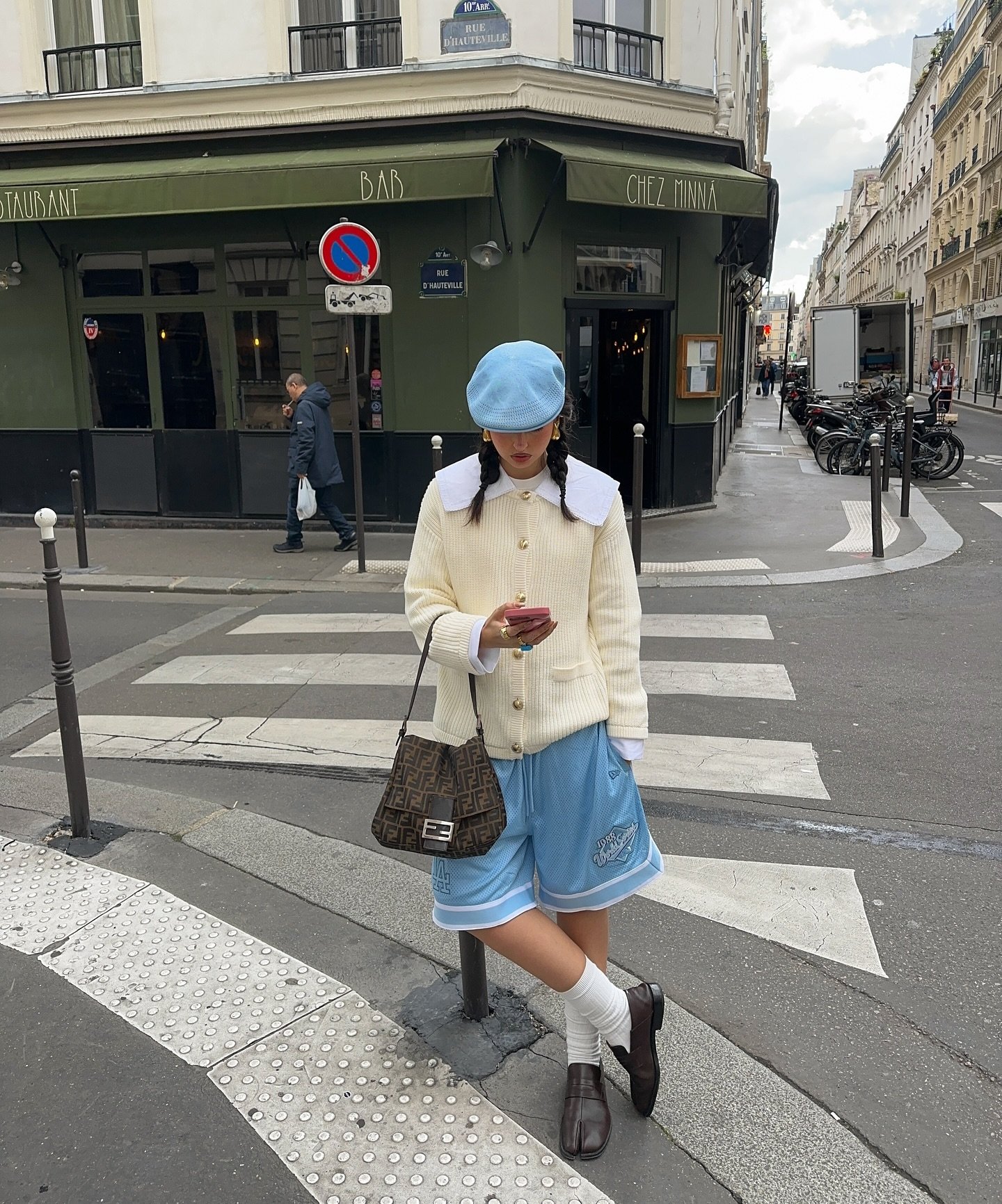 Mulher de boina azul em rua parisiense, usando loafers tendência com meias brancas e bolsa de grife.