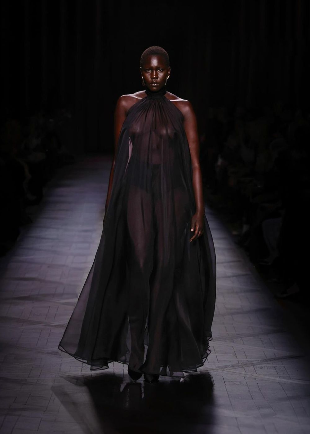 Modelo em vestido preto translúcido em uma passarela escura, evocando um estilo Romance Dark.