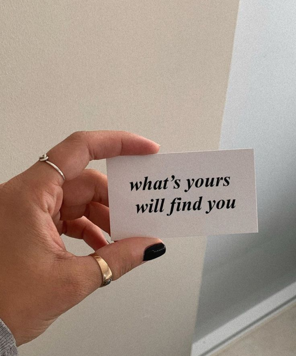 Cartão com a frase “what's yours will find you” em mãos, simbolizando destino e significado pessoal.